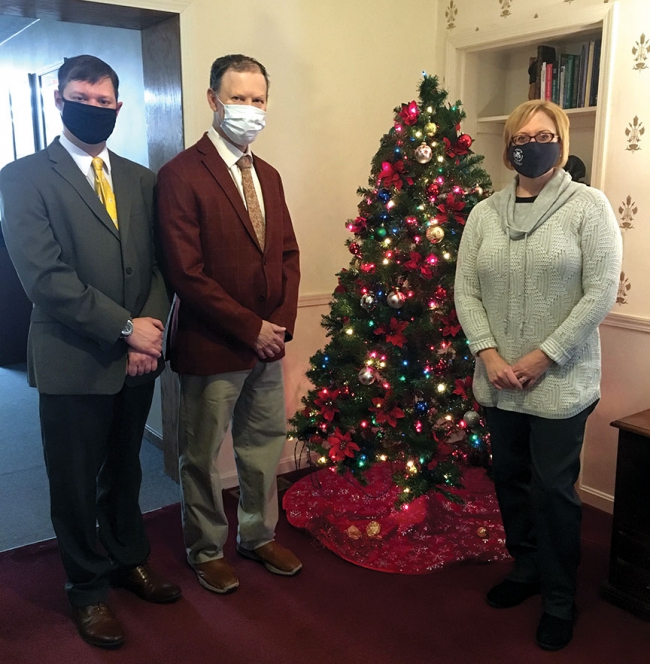 Two men and a woman next to a Christmas tree